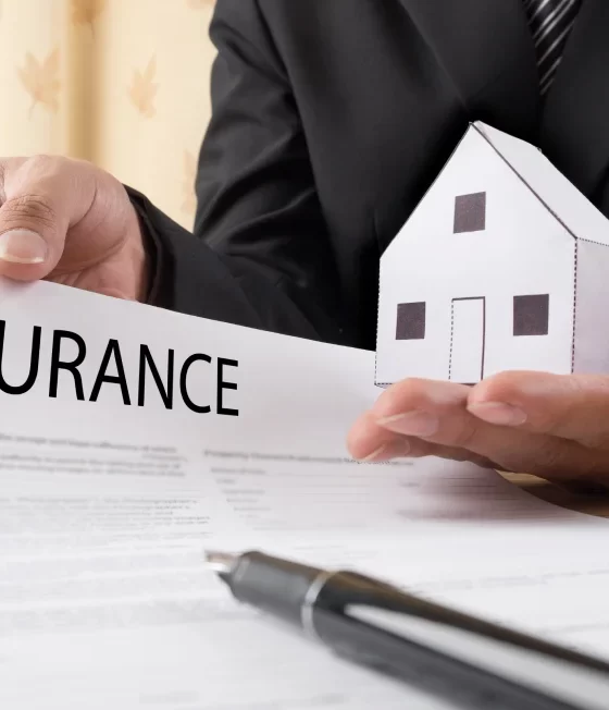 Insurance agent showing insurance policy and holding a home on his hand.