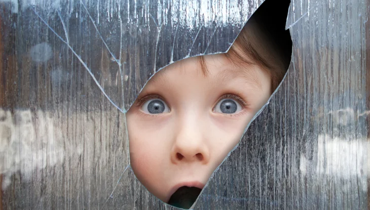 Surprised young boy looks through a hole in the window.