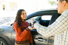 Teen receiving car keys from an adult next to a vehicle, a moment that reflects Car Insurance for Teen Drivers when starting to drive independently.