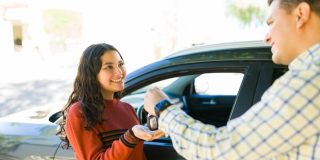 Teen receiving car keys from an adult next to a vehicle, a moment that reflects Car Insurance for Teen Drivers when starting to drive independently.