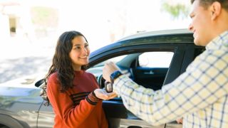 Teen receiving car keys from an adult next to a vehicle, a moment that reflects Car Insurance for Teen Drivers when starting to drive independently.