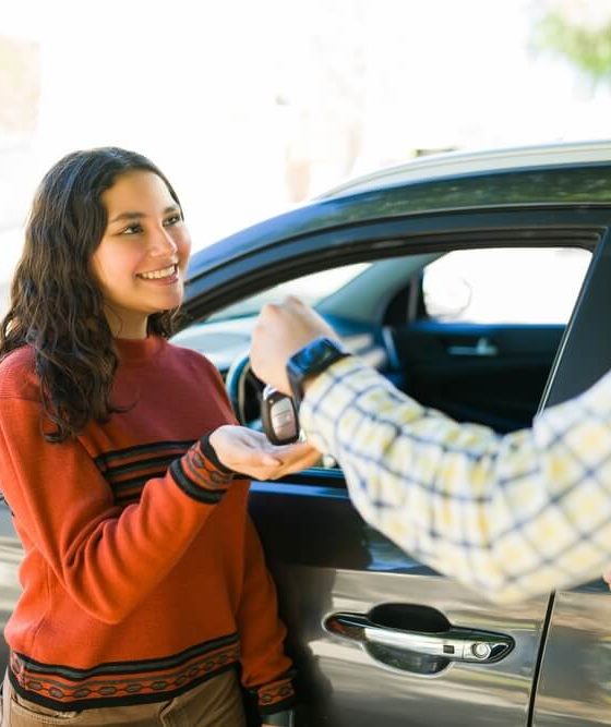 Teen receiving car keys from an adult next to a vehicle, a moment that reflects Car Insurance for Teen Drivers when starting to drive independently.