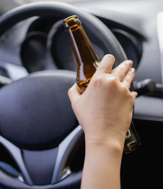 Man behind the wheel of a car with a bottle of beer.