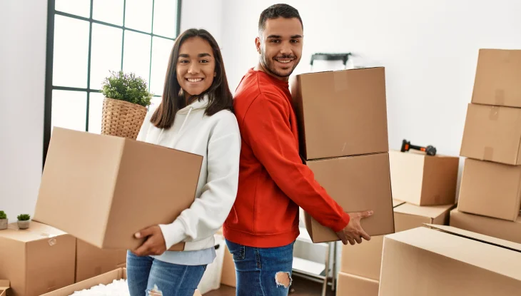 Young couple of Latinos smiling happily holding the cardboard box in their new home.