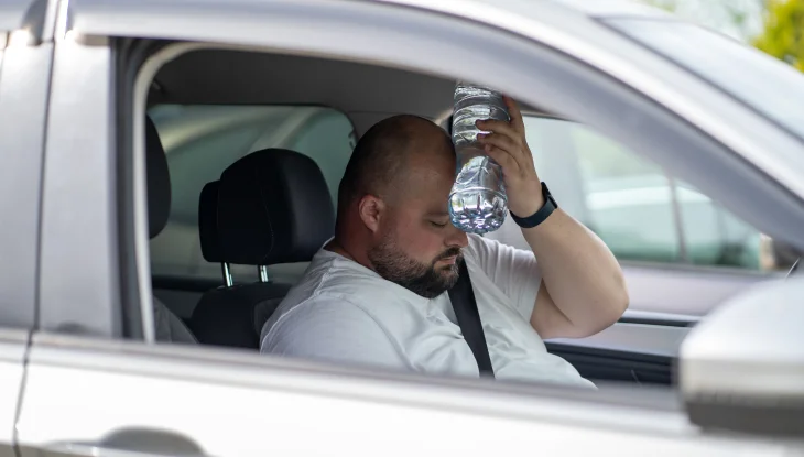 Man is using water bottle to cool off while sitting in car.