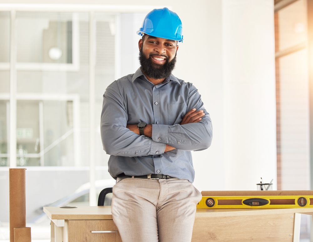 Smiling African-American contractor leans against his work table wearing blue hard hat - business insurance in Georgia