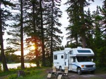 RV set up on a beautiful lake in the pine trees with chairs outside, cheap RV insurance in Georgia.
