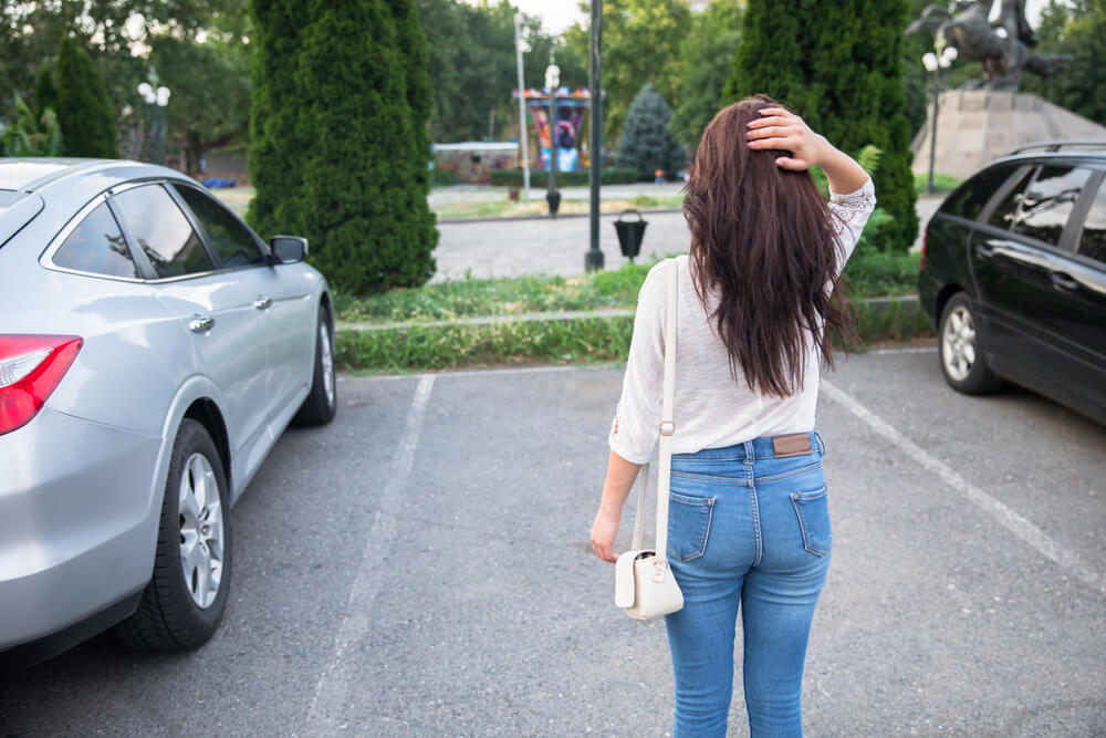 Young woman looks at parking space where her car was parked and is now gone - cheap car insurance in Georgia.