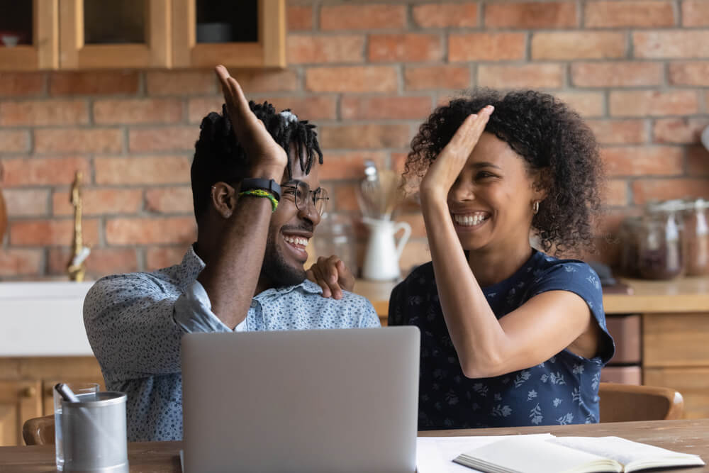 Happy black couple exchanges high five after finding cheap car insurance online.