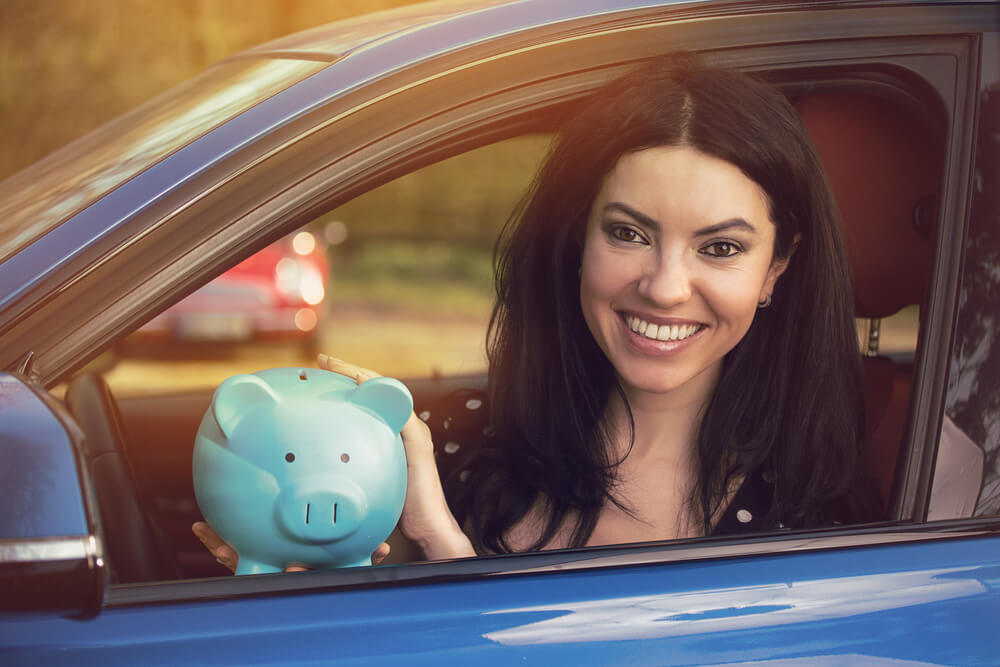 Driver inside her vehicle with a piggy bank happy to have saved thanks to Velox Insurance.
