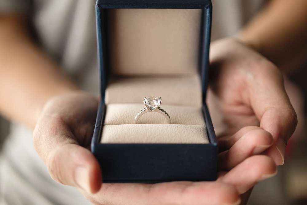 Hands holding diamond engagement ring in jewelry box