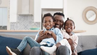 African-American father with his two children playing in the living room.