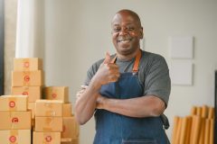 Black man business owner thumbs up with apron on in front of boxes.