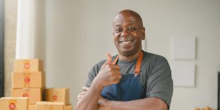 Black man business owner thumbs up with apron on in front of boxes.