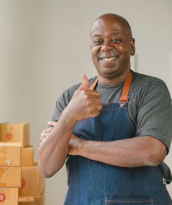 Black man business owner thumbs up with apron on in front of boxes.