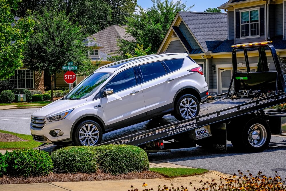 Tow truck taking silver SUV out of driveway.