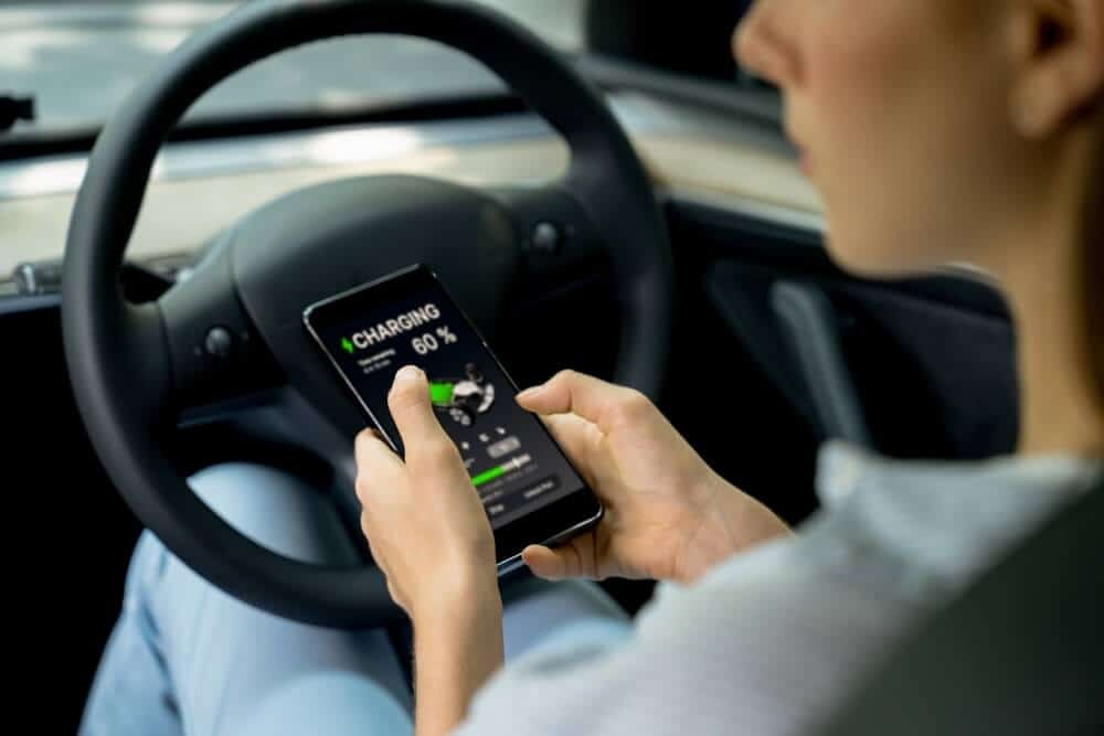 A female driver uses her phone to check the battery status of her electric vehicle - cheap insurance in Atlanta, GA.