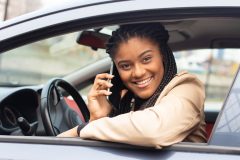 College student female looks smiling out the window of her car, sits behind wheel - cheap car insurance in Georgia.