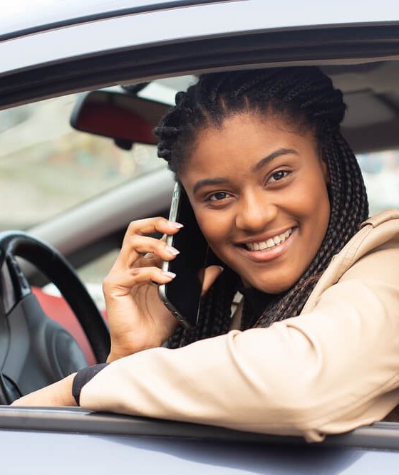 College student female looks smiling out the window of her car, sits behind wheel - cheap car insurance in Georgia.