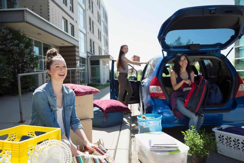 Female college students unload their belongings from a car to move into the dorm - cheap car insurance in Georgia.