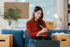 Woman sits on couch and conducts a home inventory of her belongings - cheap home insurance in Georgia.