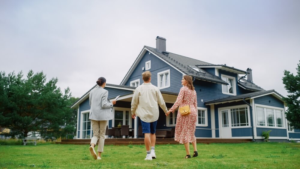 A young couple walks with a real estate agent up to a large home - cheap home insurance in Georgia.