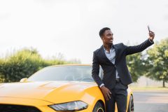 Handsome young man takes a selfie in front of his sports car - cheap car insurance in Georgia.