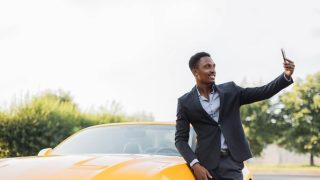 Handsome young man takes a selfie in front of his sports car - cheap car insurance in Georgia.