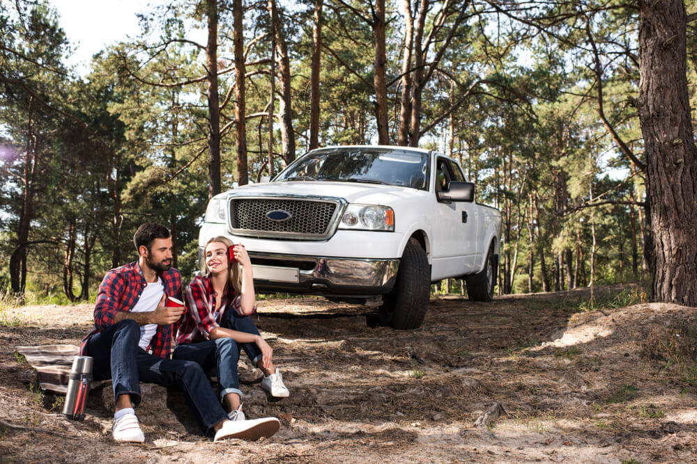 Man and woman sit on the ground in the woods with a pickup truck parked behind them - cheap car insurance in Georgia.