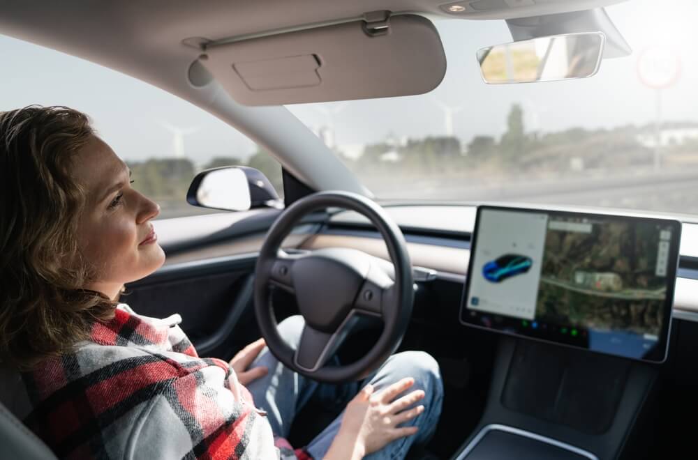 A woman sits behind the wheel of her car and enjoys self-driving technology - cheapest car insurance in Georgia.