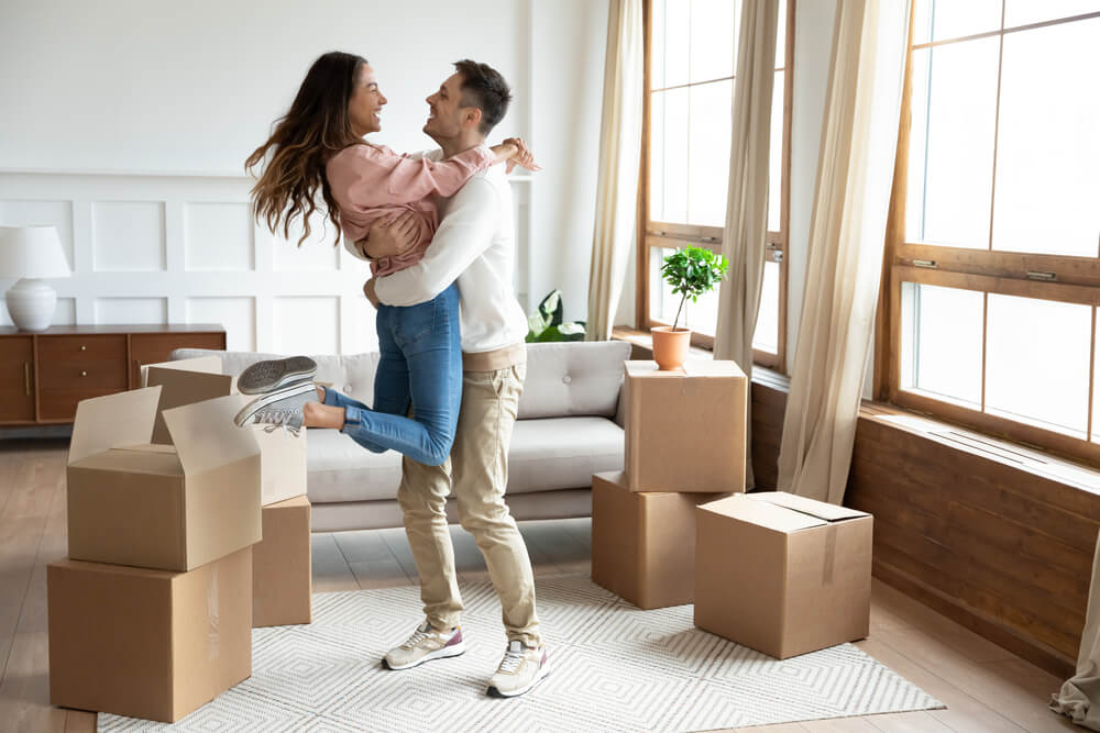 A young couple dances in their new living room of the home they just bought - cheap homeowners insurance in Georgia.