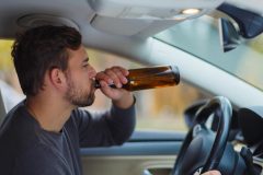 Man behind the wheel drinks from a bottle of beer, concept of high-risk driver - cheap high-risk car insurance in Georgia.