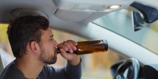 Man behind the wheel drinks from a bottle of beer, concept of high-risk driver - cheap high-risk car insurance in Georgia.