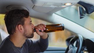 Man behind the wheel drinks from a bottle of beer, concept of high-risk driver - cheap high-risk car insurance in Georgia.