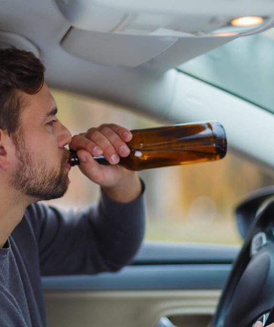 Man behind the wheel drinks from a bottle of beer, concept of high-risk driver - cheap high-risk car insurance in Georgia.