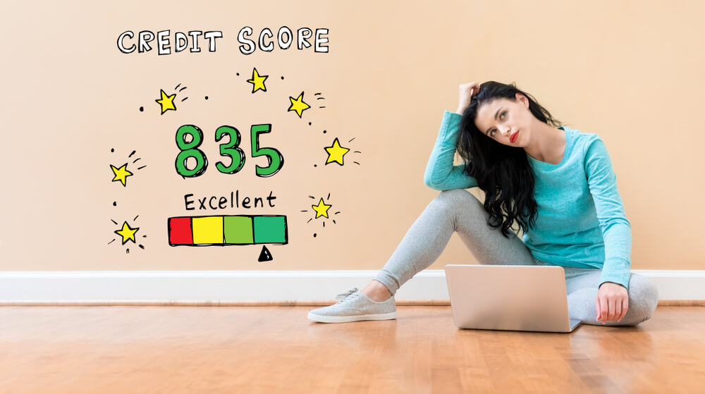 A young lady sits on the floor and ponders her credit score and what she can do with it, looking at her laptop.