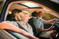 An older black man and his partner driving and smiling, biracial couple driving.
