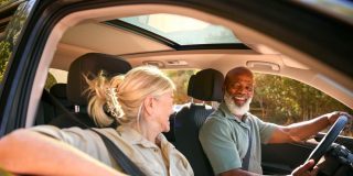 An older black man and his partner driving and smiling, biracial couple driving.