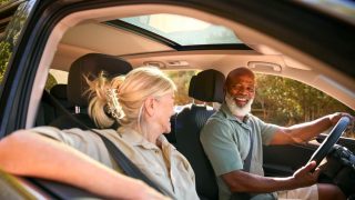 An older black man and his partner driving and smiling, biracial couple driving.