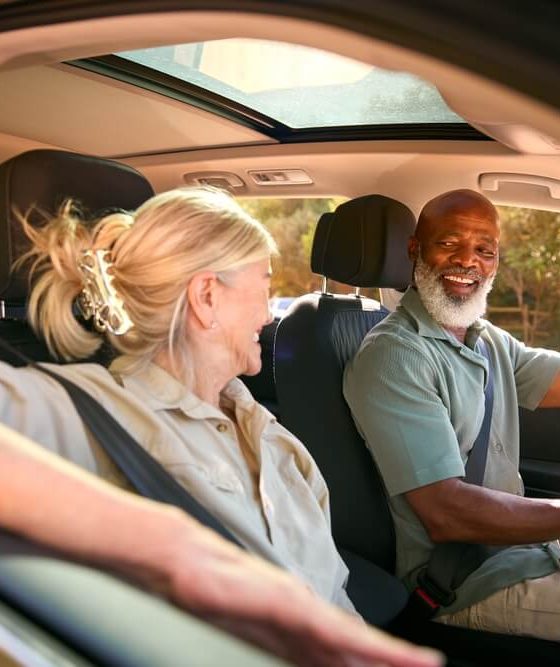 An older black man and his partner driving and smiling, biracial couple driving.