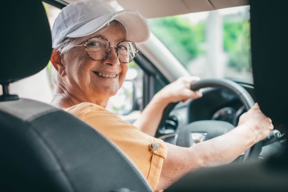 Smiling senior woman driver behind the wheel, wearing a ball cap.