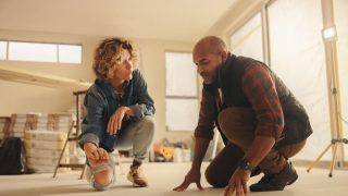 Collaborative couple working together on a DIY home renovation, discussing and planning flooring upgrades in the kitchen. How home renovation affects home insurance.
