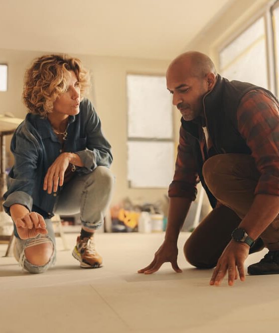 Collaborative couple working together on a DIY home renovation, discussing and planning flooring upgrades in the kitchen. How home renovation affects home insurance.