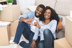 Young couple sits among the boxes, moving into their new home, building up home equity and using home insurance to help.