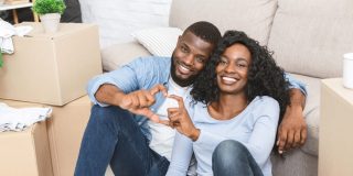 Young couple sits among the boxes, moving into their new home, building up home equity and using home insurance to help.