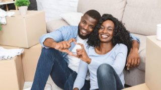 Young couple sits among the boxes, moving into their new home, building up home equity and using home insurance to help.