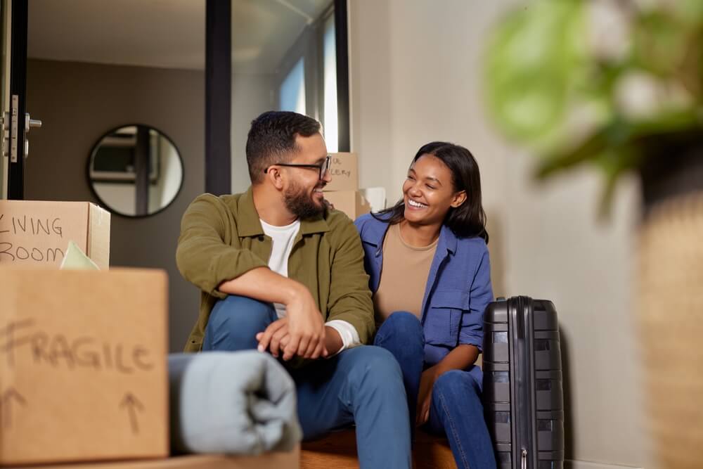 Smiling man and woman sitting on the floor after a day of moving into their new home, choosing the right home insurance deductible. 