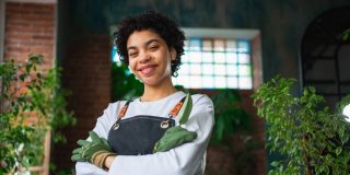 Running of own business. Woman florist wearing apron in botanical store with green plants. Happy small business owner working at flower shop smiling surrounded by plants, protected by cheap business insurance in Georgia.