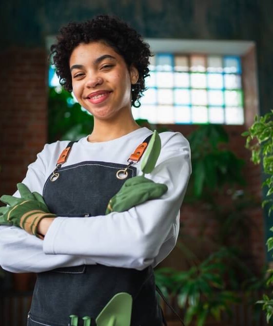 Running of own business. Woman florist wearing apron in botanical store with green plants. Happy small business owner working at flower shop smiling surrounded by plants, protected by cheap business insurance in Georgia.