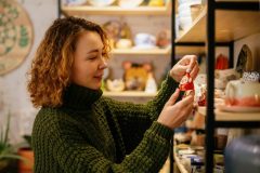 Woman in a green knit sweater choosing a handmade ceramic Christmas decoration in a festive shop, representing a small business insured for the season